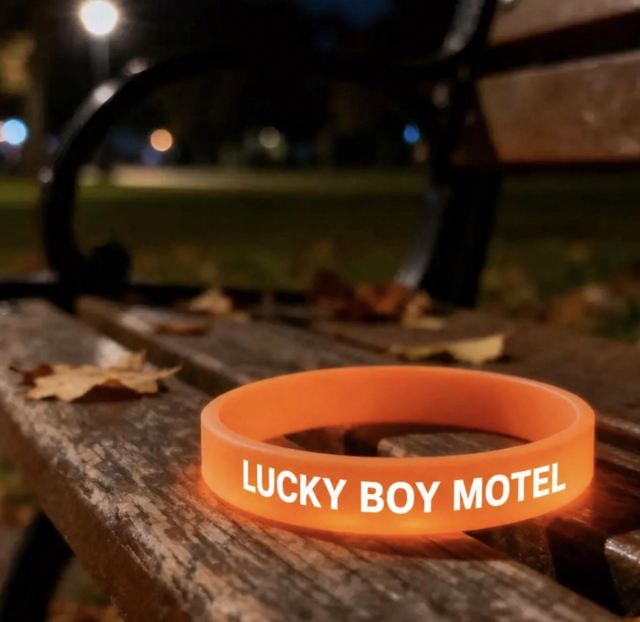 Orange glowing Lucky Boy Motel wristband on a bench at night.
